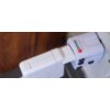 Na zdjęciu widoczny jest biały adapter podróżny SKROSS podłączony do gniazdka elektrycznego, z logo SKROSS i napisem "DESIGNED IN SWITZERLAND". Adapter ma kilka czarnych suwaków do regulacji wtyczek.