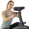 Osoba w szarej koszulce reguluje wysokość siodełka na rowerze magnetycznym. Siodełko jest czarne z zielonymi przeszyciami, a rower ma ciemną, błyszczącą ramę.