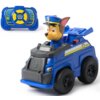 Zdalnie sterowany samochód w kolorze niebieskim z figurką psa w policyjnym mundurze na siedzeniu, obok znajduje się niebieski pilot z żółtymi przyciskami i logo "PAW Patrol". Na boku samochodu widoczny jest numer "02" oraz emblemat w kształcie gwiazdy.