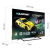 Na zdjęciu widoczny jest telewizor marki BLAUPUNKT z ekranem wyświetlającym żółty samochód wyścigowy oraz twarz kierowcy w kasku. Na ekranie znajdują się napisy: "BLAUPUNKT", "Google TV", "4K", "QD-MiniLED", "Dolby Vision IQ", "55”", "MBG7000", a także wy