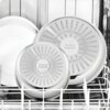 Na zdjęciu widoczne są dwie patelnie z zestawu TEFAL Ingenio Emotion umieszczone w zmywarce, obok białych talerzy. Na spodzie patelni znajduje się napis: "Tefal ingenio" oraz informacje o technologii i materiale.