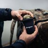 Na zdjęciu widać ręce trzymające echosondę wędkarską, którą wkładają do czarnego pokrowca z napisem "deeper". W tle znajduje się plecak w kamuflażu.