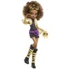 Na zdjęciu znajduje się lalka z serii Monster High, ubrana w czarną bluzkę i spódnicę z wzorem w złote cętki. Lalka ma fioletowe rękawiczki, fioletowe buty na platformie oraz złote akcesoria, w tym naszyjnik i opaskę na włosy.