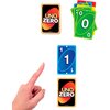 Na zdjęciu widoczna jest gra karciana "UNO Zero" z kartami w różnych kolorach, w tym zieloną kartą z numerem "0" i niebieską kartą z numerem "1". Obok kart znajduje się ręka wskazująca na niebieską kartę, a na odwrocie kart widnieje logo "UNO Zero".
