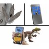 Na zdjęciu widoczny jest zestaw figurek z serii Jurassic World, w tym welociraptor oraz elementy interaktywne, takie jak aplikacja na smartfonie i pilot z niebieskimi przyciskami. Na spodzie łapy dinozaura znajduje się czarno-biały wzór przypominający kod