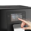Czarny ekspres do kawy z dotykowym panelem, na którym widoczne są opcje wyboru napojów: "RISTRETTO", "ESPRESSO", "LONG COFFEE", oraz godzina 18:04 i ikona ulubionych. Palec wskazujący dotyka ekranu, wybierając opcję "ESPRESSO".