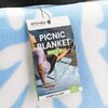 Etykieta na kocu piknikowym przedstawia napis "SPOKEY LIVE WITH PASSION!" oraz "PICNIC BLANKET BREEZE XL", a także informacje w kilku językach: "KOC PIKNIKOWY, PIKNIKOVÁ DEKA, PICKNICKDECKE" i wymiary "210 x 150 cm". Na dole widnieje napis "COMFY & COZY".