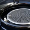 Na zdjęciu znajduje się kuchenka turystyczna z czarną powierzchnią grillową, na której leżą kawałki mięsa i sera. Obok kuchenki widoczne są talerze z różnymi potrawami oraz szklanka z napojem, a na panelu kuchenki widnieje logo producenta EXTRALINK.