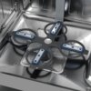 Wnętrze zmywarki z widocznym metalowym ramieniem spryskującym w kształcie krzyża, z niebieskimi i srebrnymi elementami, oraz metalowym filtrem na dnie. Ściany zmywarki są wykonane ze stali nierdzewnej, z widocznymi panelami i odbiciami światła.