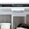 Wnętrze lodówki z widocznym napisem "purebeam+" na górnym panelu, poniżej znajduje się biały pojemnik z pokrywką oraz liście sałaty. W tle widać półprzezroczyste drzwi lodówki.