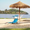 Na zdjęciu znajduje się niebieski leżak turystyczny z daszkiem, ustawiony na piaszczystej plaży. W tle widoczny jest parasol z liści palmowych, hamak oraz jezioro z zalesionym brzegiem.
