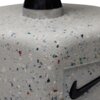 Zbliżenie na szarą hantlę z teksturą przypominającą drobne, kolorowe plamki. Widoczne jest czarne logo Nike na powierzchni hantli.