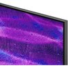 Przestronny salon z dużym telewizorem zamontowanym na ścianie, wyświetlającym kolorowy, abstrakcyjny obraz w odcieniach fioletu i niebieskiego. Przed telewizorem znajduje się nowoczesny stolik z dekoracjami, a po obu jego stronach ustawione są dwa brązowe