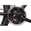 Zbliżenie na mechanizm korbowy roweru górskiego z widocznym napisem "Cyclone" na ramieniu korby oraz "Shimano Tourney" na przerzutce. Łańcuch jest napięty, a zębatki są osłonięte przezroczystą osłoną.