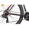 Zdjęcie przedstawia zbliżenie na mechanizm napędowy roweru górskiego, ukazując łańcuch, zębatki oraz przerzutkę z widocznym napisem "Shimano Tourney". Opona roweru jest szeroka, z wyraźnym bieżnikiem, a rama ma czarno-czerwone wykończenie.