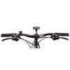 Na obrazie widoczna jest kierownica roweru górskiego z czarnymi uchwytami o wzorze zygzakowatym oraz dźwigniami hamulcowymi i przerzutkami marki Shimano. Na środku kierownicy znajduje się odblask, a obok niego dzwonek rowerowy.