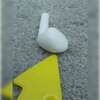 Białe słuchawki douszne leżą na szarej, teksturowanej powierzchni, obok znajduje się żółty, plastikowy element.