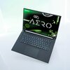Na zdjęciu znajduje się otwarty laptop z widocznym ekranem, na którym wyświetlany jest napis "AERO" oraz logo "GIGABYTE" w lewym górnym rogu. Klawiatura laptopa jest czarna, a tło ekranu ma zielono-czarne elementy graficzne z napisem "PLAY TO DIFFER."