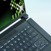 Na zdjęciu widoczna jest klawiatura laptopa z podświetleniem oraz fragment ekranu z zielono-czarnym wzorem i srebrnym elementem. Na klawiaturze znajdują się klawisze funkcyjne od F1 do F12 oraz inne standardowe klawisze.
