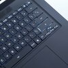 Zbliżenie na klawiaturę laptopa z podświetlanymi klawiszami, na których widoczne są symbole i litery, takie jak "F9", "F10", "Ctrl", "Alt Gr", oraz klawisze strzałek. Klawiatura ma ciemną obudowę, a podświetlenie klawiszy jest w kolorze niebieskim.