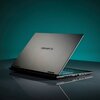 Na zdjęciu widoczny jest laptop z częściowo otwartą pokrywą, na której znajduje się logo "GIGABYTE". Urządzenie stoi na gładkiej powierzchni, a w tle widać jednolite, ciemnozielone tło.