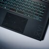 Na zdjęciu widoczna jest klawiatura laptopa z podświetleniem w kolorze niebieskim oraz duży touchpad. W prawym dolnym rogu obudowy znajduje się napis "GAMING".
