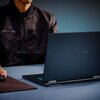 Na zdjęciu widoczny jest otwarty laptop z logo "GIGABYTE" na obudowie, ustawiony na biurku. Obok laptopa znajduje się osoba w ciemnej kurtce, trzymająca myszkę na podkładce.