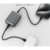 Szary powerbank z podłączonymi dwoma urządzeniami, jednym przez kabel USB-C, a drugim przez USB-A; nad powerbankiem widoczny jest napis "USB-C x 1 / USB-A x 1". Na powierzchni powerbanku znajdują się cztery diody LED oraz przycisk.