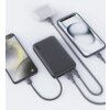 Na zdjęciu widoczny jest szary powerbank z logo "AUKEY", do którego podłączone są dwa smartfony i etui na słuchawki bezprzewodowe. Na ekranie jednego z telefonów widnieje godzina 8:30 i data "August 18th".