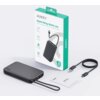 Na zdjęciu znajduje się szary powerbank z napisem "AUKEY" oraz "10000" na obudowie, obok którego leży kabel USB-C i karta gwarancyjna. W tle widoczny jest zielono-biały karton z napisem "AUKEY Spark Sling 10000 Lite" oraz grafiką przedstawiającą powerbank