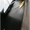 Zdjęcie przedstawia fragment czarnego okapu kuchennego z metalowym filtrem i żółtą strzałką wskazującą na jego powierzchnię. W tle widoczna jest szara powierzchnia, prawdopodobnie podłoga.