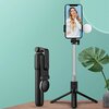 Na zdjęciu znajduje się czarny uchwyt selfie z rozłożonymi nóżkami, na którym zamocowany jest smartfon z wyświetlonym zdjęciem osoby w kwiecistej sukience. W tle widoczne są trzy okrągłe wstawki pokazujące różne zastosowania uchwytu, w tym poziome ustawie