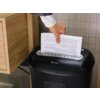 Osoba wkłada kartkę papieru z tekstem do czarnej niszczarki z widocznym logo "tracer" na obudowie. Niszczarka znajduje się obok drewnianej szafki.