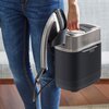 Osoba trzyma system do prasowania z widocznym napisem "Tefal Ixeo Power" na urządzeniu. Produkt ma metaliczny uchwyt i czarną podstawę, a w tle widać fragment sofy i podłogi.