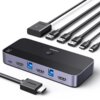 Na zdjęciu znajduje się przełącznik KVM marki UGREEN z kilkoma portami HDMI i USB, a także zestaw kabli z wtyczkami USB i HDMI. Na urządzeniu widoczne jest logo "UGREEN" oraz oznaczenie "4K 60Hz".