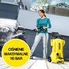 Żółta myjka ciśnieniowa z napisem "KARCHER" stoi na zewnątrz obok osoby myjącej samochód, a na zdjęciu widoczny jest żółty okrąg z tekstem "CIŚNIENIE MAKSYMALNE 110 BAR". W tle znajduje się nowoczesny budynek i drzewa.