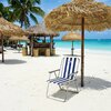 Na zdjęciu znajduje się niebiesko-białe krzesło turystyczne z napisem "NILS CAMP" na tle piaszczystej plaży z turkusowym morzem. Wokół krzesła widoczne są słomiane parasole oraz drewniany bar, a w tle rosną palmy.