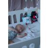 Na zdjęciu widać niemowlę śpiące w białym łóżeczku, obok którego znajduje się przytulanka HENCZ TOYS Króliczek Moms Care oraz zawieszone na łóżeczku ozdoby w kształcie gwiazdek i chmurki. Dziecko ma smoczek w buzi i leży na białej pościeli z delikatnym wz