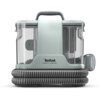 Odkurzacz w kolorze jasnoszarym z przezroczystymi elementami, na którym widnieje napis "Tefal Clean It Compact". W dolnej części urządzenia znajduje się zwinięty wąż, a z boku przymocowana jest szczotka.