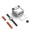 Pudełko z napisem "amazfit ACTIVE 2" znajduje się obok czarnego smartwatcha z kwadratową tarczą, dwóch wymiennych pasków w kolorze czarnym i pomarańczowym oraz instrukcji z napisem "amazfit ACTIVE 2 Square". Obok leży okrągłe urządzenie, prawdopodobnie ła