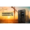 Na zdjęciu znajduje się czarny telefon komórkowy z widocznym ekranem i klawiaturą, umieszczony na tle placu budowy z dźwigami. Obok telefonu widnieje napis: "HAMMER HORIZON LTE".