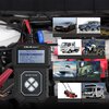Na zdjęciu znajduje się tester akumulatorów z wyświetlaczem, na którym widoczne jest menu z opcjami: "1. Quick Test, 2. Battery in Vehicle, 3. Out of Vehicle, 4. Voltmeter, 5. Review Data, 6. System Setup". Obok testera umieszczono zdjęcia różnych pojazdó