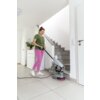 Na zdjęciu znajduje się szorowarka do czyszczenia schodów KARCHER BD 17/5 C Ep 1.737-107.0, ustawiona na podłodze przy schodach. W tle widoczna jest jasna ściana, drzwi oraz szafka z rośliną.