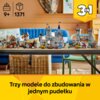Na zdjęciu znajduje się zestaw klocków LEGO przedstawiający średniowieczny zamek z różnymi elementami, takimi jak wieże i wiatrak, ustawiony na stole w domowym wnętrzu. W dolnej części zdjęcia widnieje napis: "Trzy modele do zbudowania w jednym pudełku", 