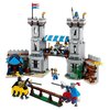 Zestaw LEGO przedstawia średniowieczny zamek z dwiema wieżami, mostem zwodzonym i kolorowymi flagami. Na pierwszym planie znajdują się dwaj rycerze na koniach, przygotowani do turnieju, a w tle widoczna jest scena z życia zamku, w tym postacie i detale ar