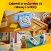 Na zdjęciu widoczny jest zestaw klocków LEGO przedstawiający niebieski telefon w stylu retro, umieszczony na drewnianym stoliku obok ołówka i żółtej notatki z napisem "LEGO 31174". W tle znajduje się kolorowy koc oraz roślina w doniczce, a na górze zdjęci