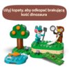 Zestaw LEGO przedstawia scenę z figurkami, drzewem i małym stawem na zielonej podstawce. Na górze znajduje się napis: "Użyj łopaty, aby odkopać brakującą kość dinozaura".