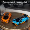 Na zdjęciu znajdują się dwa modele samochodów z klocków, jeden pomarańczowy, drugi niebieski z pomarańczowymi elementami, ustawione na okrągłej powierzchni. W górnej części zdjęcia widnieje napis: "Fani motoryzacji mogą urządzać niesamowite wyścigi".