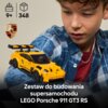 Na zdjęciu znajduje się żółty model samochodu LEGO Porsche 911 GT3 RS, obok którego widoczna jest osoba w koszuli w kratę. W górnej części zdjęcia znajdują się ikony z oznaczeniem wieku 9+ i liczby elementów 348, a także logo Porsche; na dole widnieje nap