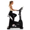 Na zdjęciu znajduje się rower elektromagnetyczny HAMMER Maximum UB 8000 z osobą siedzącą na siodełku i trzymającą kierownicę. Na obudowie roweru widoczne jest logo "HAMMER Maximum".